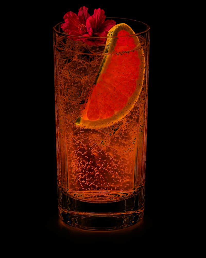 Copper Bloom tequila highball in a tall glass with sparkling grapefruit-pink tones, ice, a ruby grapefruit wedge and a hibiscus flower garnish.